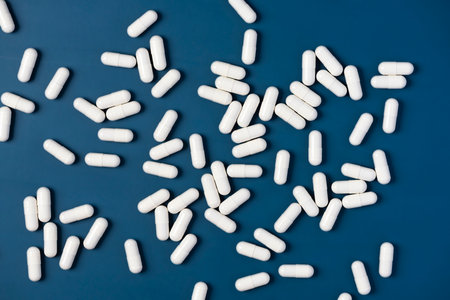 White Drug Capsules Scattered on Blue Table Top View.
