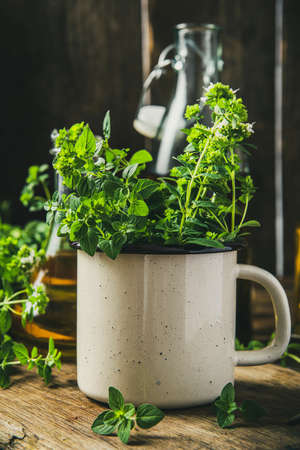 Fresh Oregano or Marjoram Bunch in Rustic Cup On Wooden Kitchen Table.の写真素材