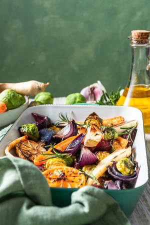 Roasted root vegetables with herbs on wooden table.