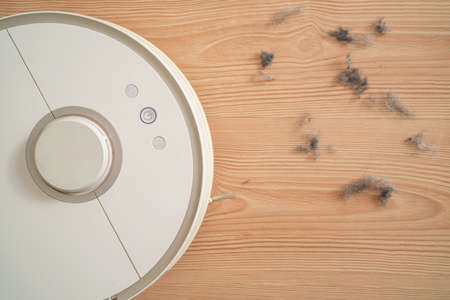 robot vacuum cleaner removes dust in room on brown floor. vacuum cleaner in ordinary apartment....