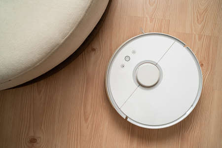 robot vacuum cleaner removes dust in room on brown floor. vacuum cleaner in ordinary apartment....