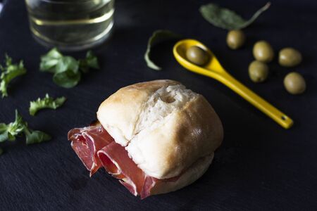 Close up appetizing muffin with serrano ham in low key with an appetizer background of olives in a...