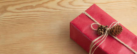 Christmas gift wrapped in recycled paper in red decorated with a rope loop with pine cones. Ecological, handmade gift and magical concept.Copy space for message and advertising.の写真素材
