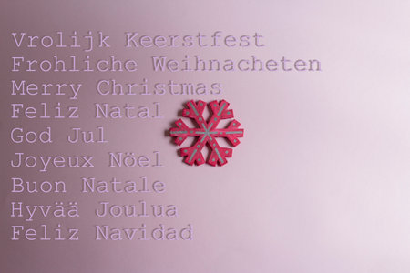 Christmas card in pink with pink snowflake decoration and Merry Christmas signs in multiple languages.の写真素材