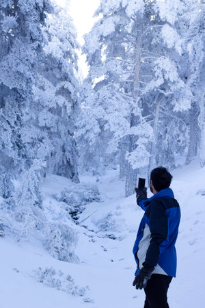 a middle-aged man searches for wifi signal on a snowy mountain. wifi connection in deep nature.の写真素材