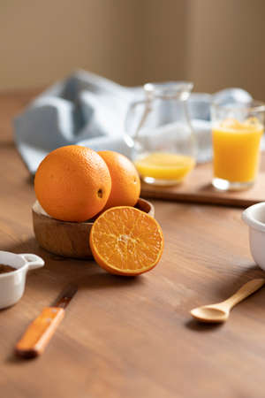 still life of bowl with oranges at breakfast on a wooden table and orange juice out of focus in the backgroundの写真素材