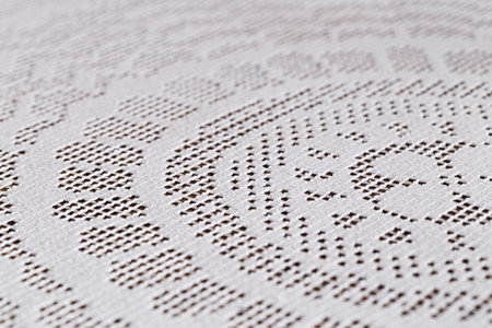 Close up of a white hand crocheted doily with geometric and circular shapes on a table. Select...