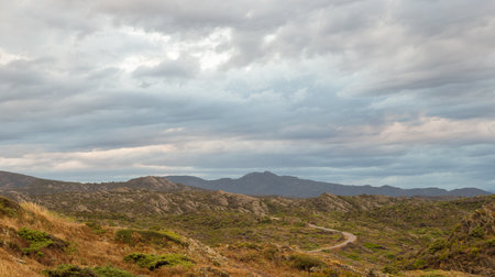 Panoramic view of the mountains of Cap de Creus on a cloudy autumn day. There is a narrow winding road.の写真素材