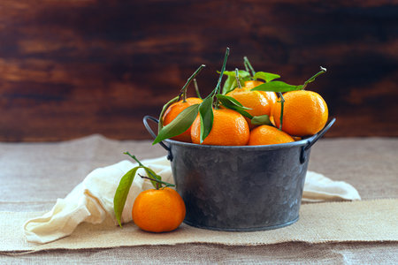 Metal basket with freshly picked tangerines. Tangerines do not have their leaves. The background is brown, there is a white napkin and sackcloth under the bowl.の写真素材