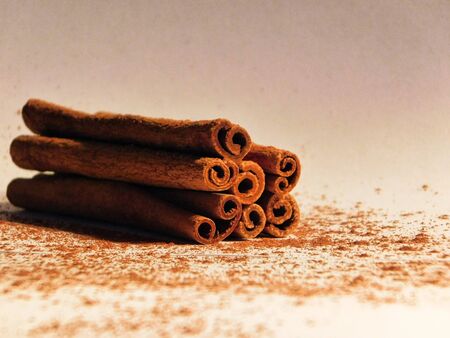 Pile of dry cinnamon sticks on white backdrop, with some cinnamon dusting