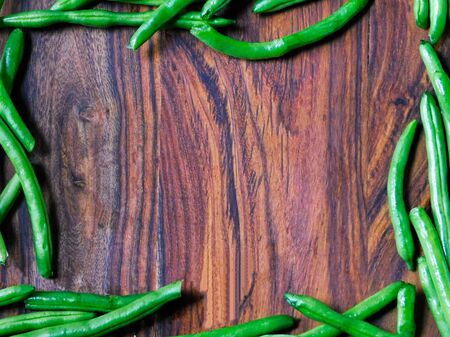 Whole green beans frame an empty space on a wooden cutting boardの写真素材