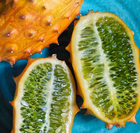 The green inside pulp of a halved kiwano fruit, on a blue plate and lit with natural sunlightの写真素材