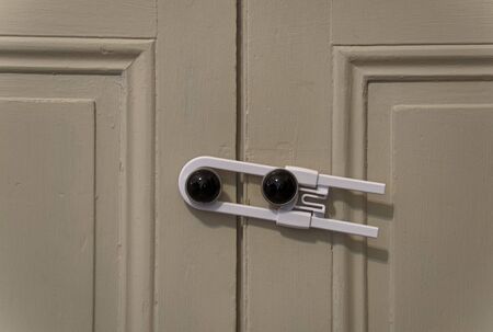 Close up view of a white child safety lock holding two cabinet doors togetherの写真素材