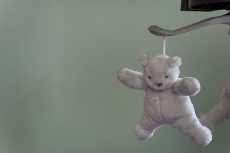 One grey, white plush teddy bear hanging from a mobile, with copy space to the leftの写真素材