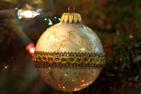 Close up view of an old fashioned white and gold Christmas bulb in the light of a white Christmas string lightの写真素材