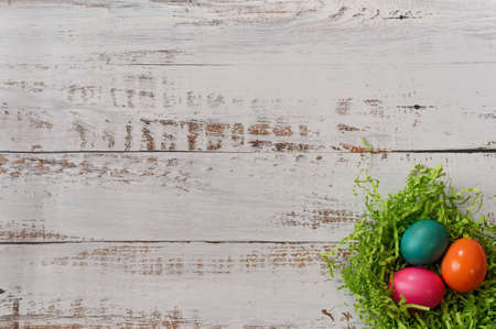 Three colorfully painted easter eggs in an easter grass nest in lower right corner of a white wooden background, with copy spaceの写真素材