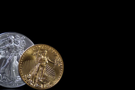 A one ounce gold coin and a one ounce silver eagle coin on a black background, with copy spaceの写真素材