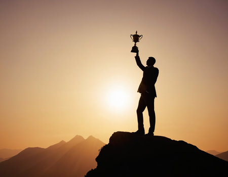 Silhouette of successful businessman with trophy on top of the mountainの素材