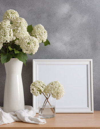 White hydrangea flowers in vase and photo frame on wooden table.の素材