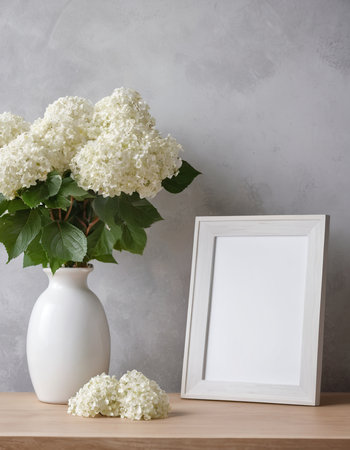 White hydrangea flowers in vase and photo frame on wooden table over gray wall.の素材