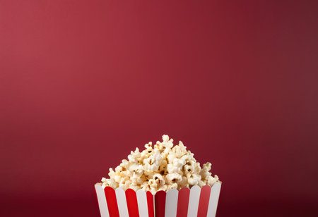 Popcorn in a striped box on a red background. Copy space.の素材