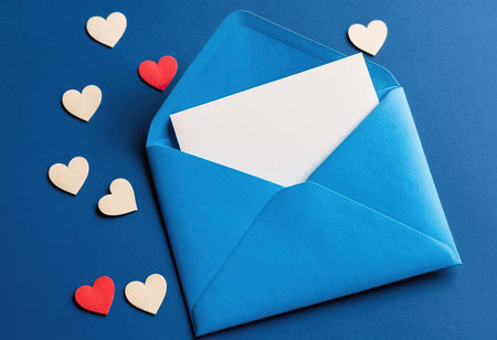 Envelope with blank card and paper hearts on blue background.の素材