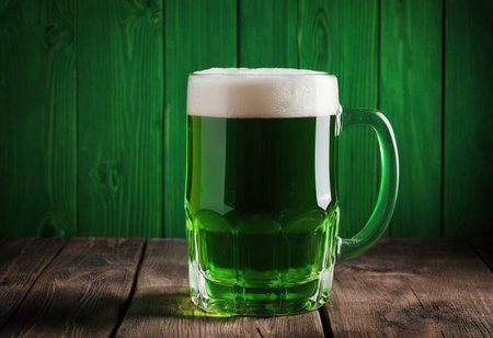 Mug of green beer on wooden table over green wooden wall backgroundの素材