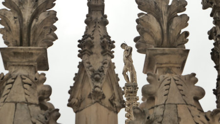 A striking statue stands prominently atop a historic structure, surrounded by intricately designed stonework. The cloudy sky forms a dramatic backdrop, emphasizing the architectural beauty.の写真素材