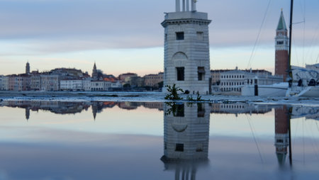 Calm waters reflect historic buildings in Venice during dawn, highlighting the city's architecture and a peaceful morning atmosphere. The soft light enhances the scenic beauty.の写真素材