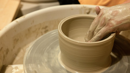 A skilled potter carefully forms a bowl from wet clay on a spinning wheel in a cozy studio. The ambiance is artistic and focused, highlighting craftsmanship.の写真素材