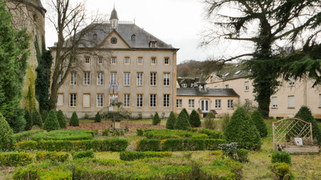 A charming historic building stands adjacent to an elegant garden filled with neatly trimmed hedges and benches, showcasing the beauty of early spring in a calm village.の写真素材