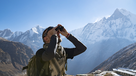 Hiker looking through binoculars on a trekking trail to the Annapurna base camp, the Himalayas, Nepal. Himalayas mountain landscape in the Annapurna region. Snowy mountains, high peaks of Annapurnaの写真素材