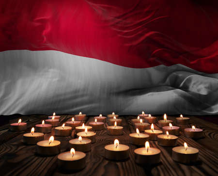 Mourning candles burning on Indonesia national flag of background. Memorial weekend, patriot veterans day, National Day of Service & Remembrance. Burning candles on wooden surface. 3d illustration.の写真素材
