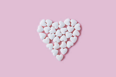 Concept of heart pills. Small white pills scattered in the shape of a heart on a pink background. Pills for heart disease. Medical banner, copy space, place for text.の写真素材