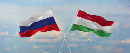 flags of Russia and Hungary waving in the wind on flagpoles against sky with clouds on sunny day. Symbolizing relationship, dialog between two countries. 3d illustration,の写真素材