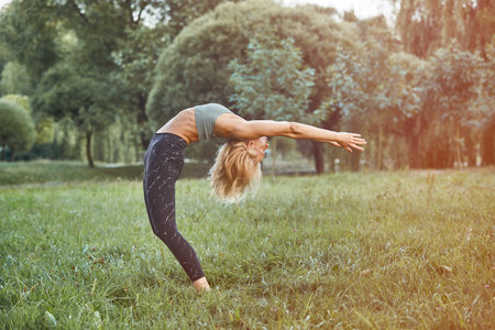 young Sport blond woman yogini practice yoga exercise in park on evening, sunset. yoga is meditation and healthy sport concept.の写真素材