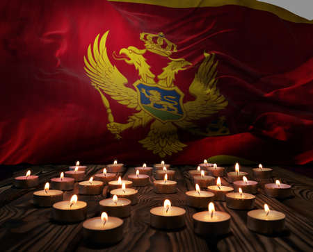 Mourning candles burning on Montenegro national flag of background. Memorial weekend, patriot veterans day, National Day of Service Remembrance. Burning candles on wooden surface. 3d illustration.の写真素材