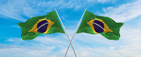 crossed national flags of Brazil  and Brazil flag waving in the wind at cloudy sky. Symbolizing relationship, dialog, travelling between two countries. Copy space. 3d illustrationの写真素材