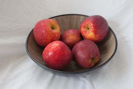 Four red apples in a bowl, on a white background.