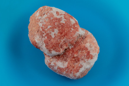 Two hamburger patties thawing on blue plate