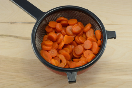 Rinsed sliced canned carrots draining in strainer in bowl to remove salt on wooden tableの写真素材