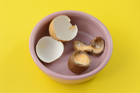 Broken Easter chocolate cream egg with broken eggshells in pink dish against yellow backgroundの写真素材