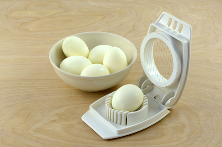 Peeled whole hard boiled eggs in bowl and one in egg slicerの写真素材