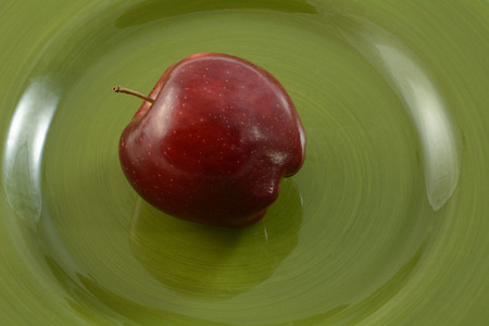 Close of of whole raw Red Delicious apple on green plateの写真素材