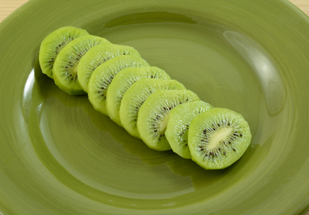 Close up of sliced kiwi fruit on green plate as snack or in preparation to be used as cooking ingredientの写真素材