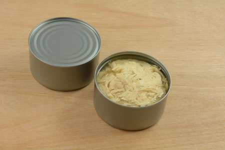 Two cans of albacore tuna fish with one can opened on wooden tableの写真素材