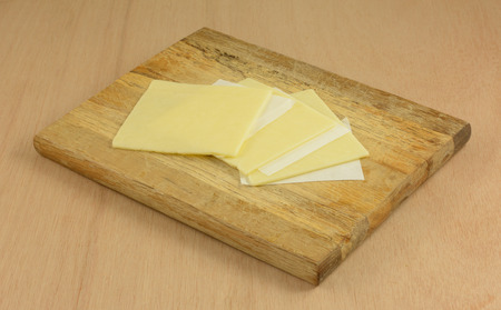 Close up of white cheddar cheese slices separated by paper on wooden cutting board in preparation for making foodの写真素材