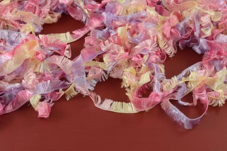 Background of strands of pastel colored yellow red and purple yarn or ribbon on red wood
