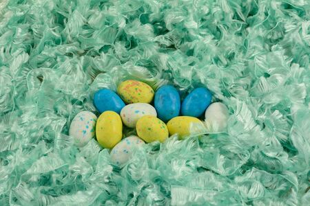 Candy covered malted milk for Easter in shape of bird eggs in nest of soft fluffy green ribbon
