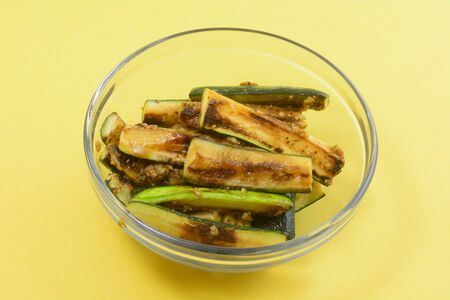 Roasted fresh zucchini squash spears with garlic in glass bowl on yellow backgroundの写真素材